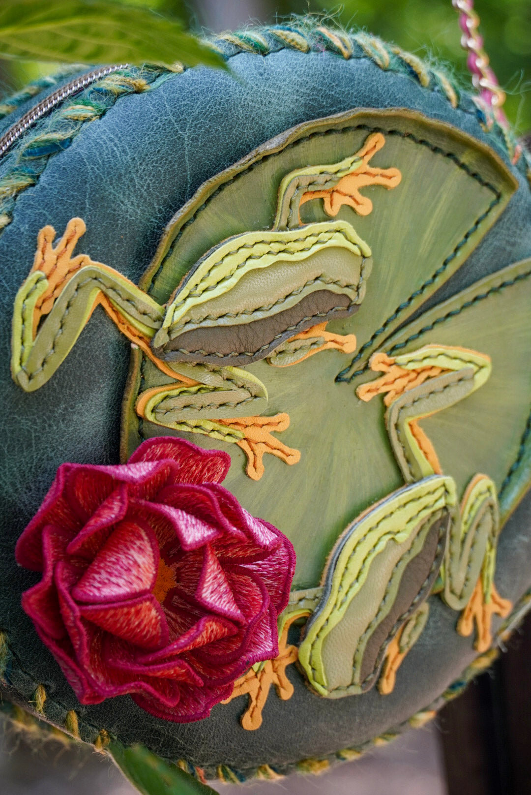 Embroidered leather piece with frogs and a flower on a textured background